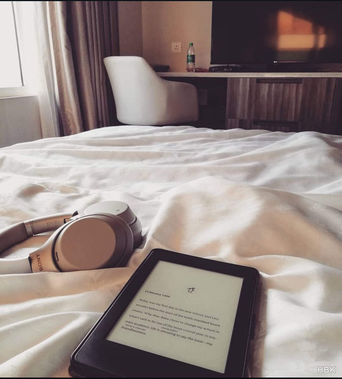 Headphones and an e-reader resting on a bed beside a window